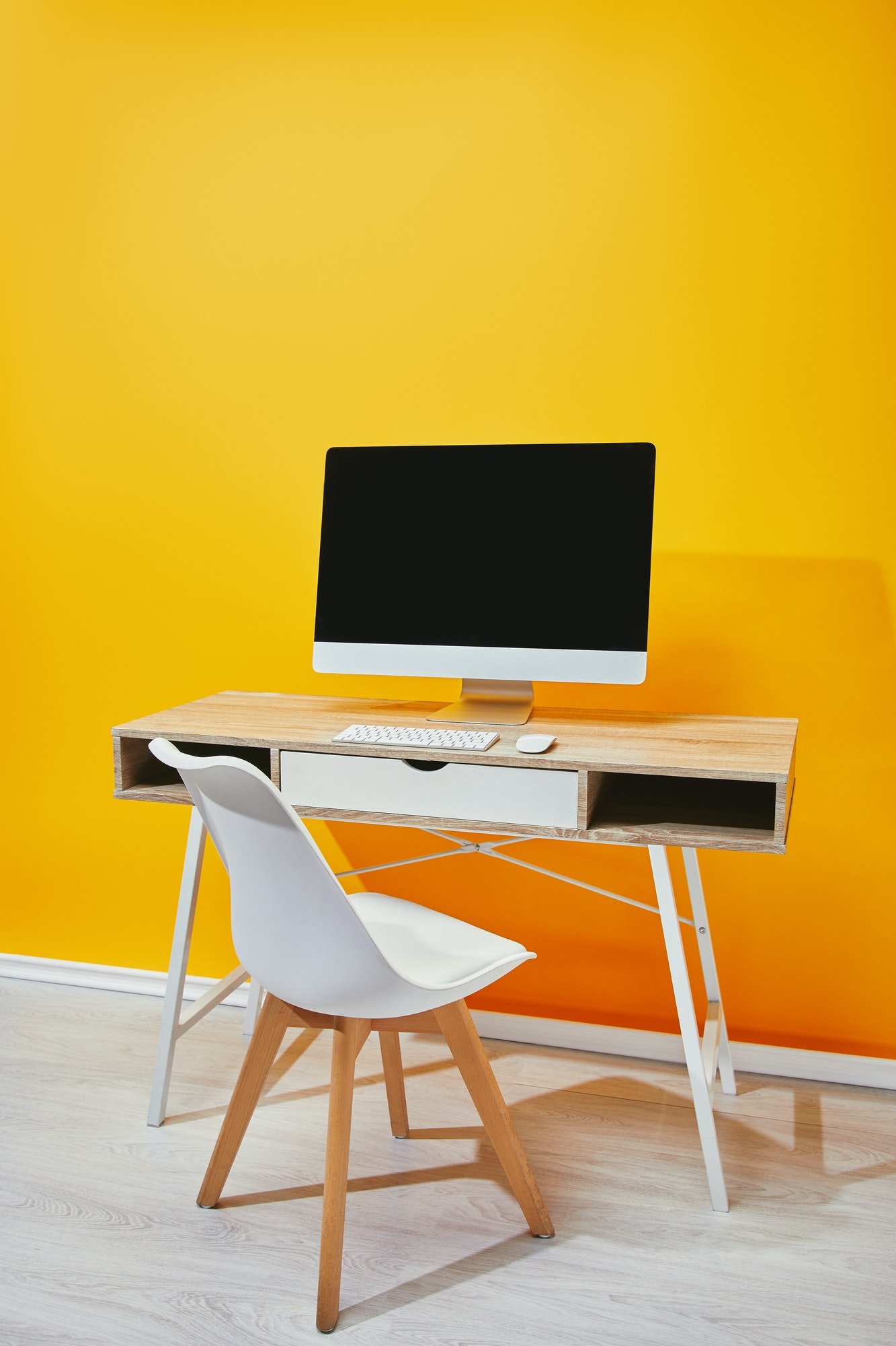 Computer with blank screen at wooden table and chair near yellow wall